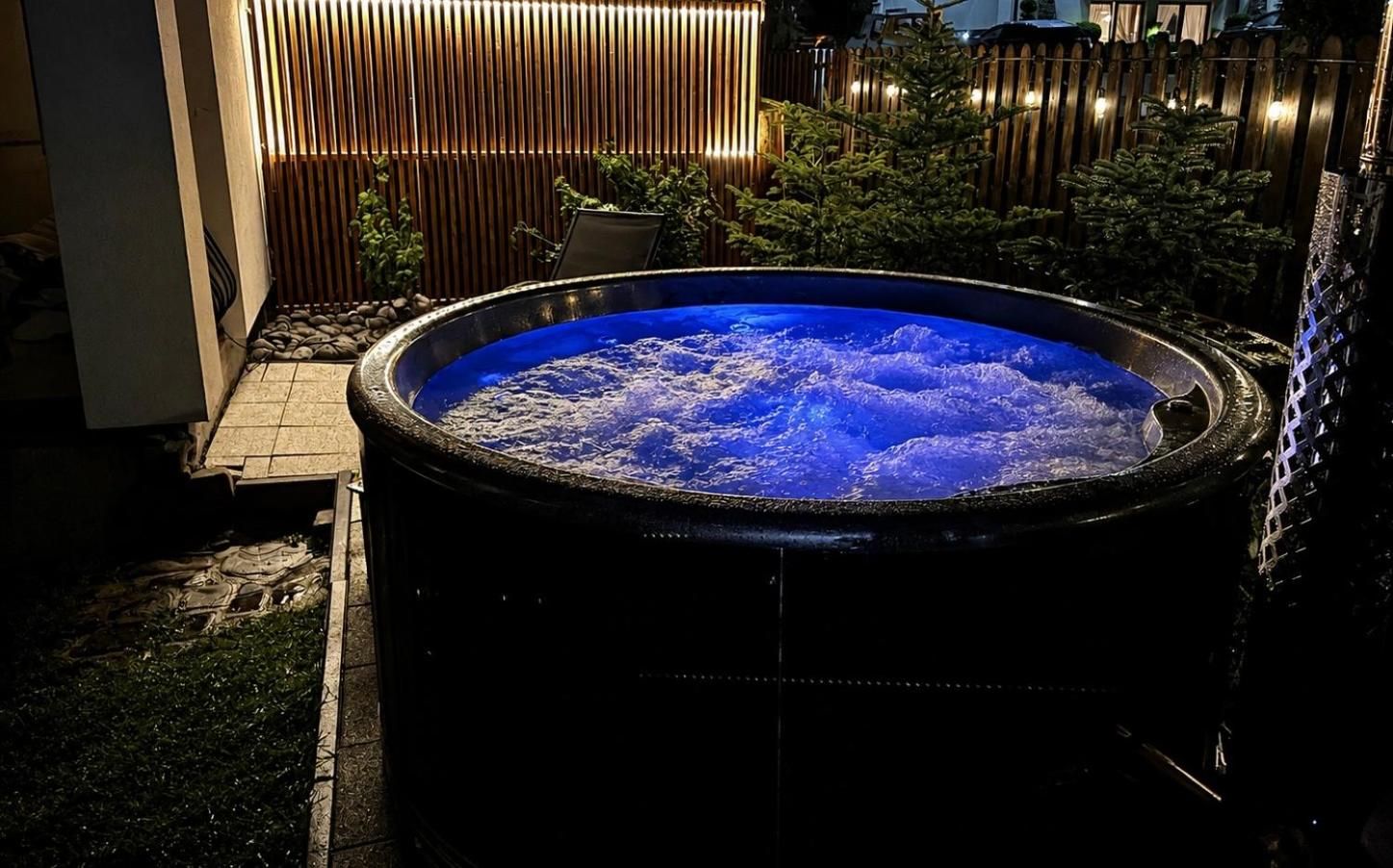 Jacuzzi z niebieskim podświetleniem nocą, za nim podświetlony drewniany parawan